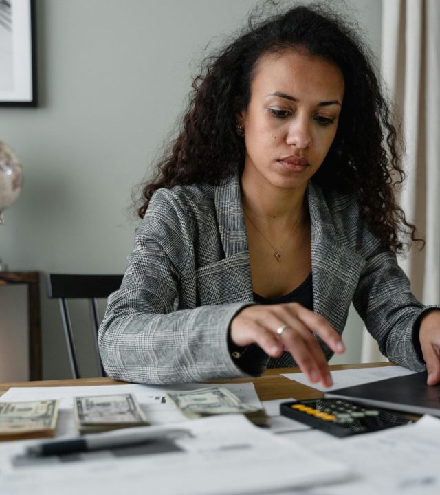 Professional woman analyzing financial documents and counting cash at office desk.