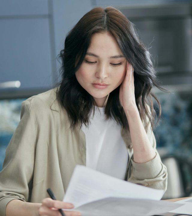 Young woman reviewing paperwork at home, focused and concerned.